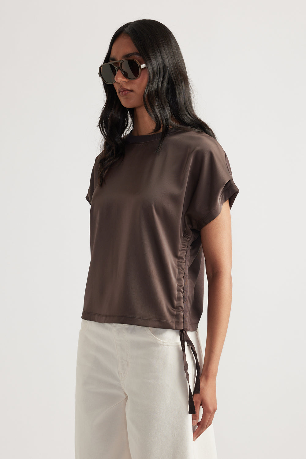 Woman wearing a relaxed fit short sleeve top with ruched side tie detail paired with light-colored wide-leg pants
