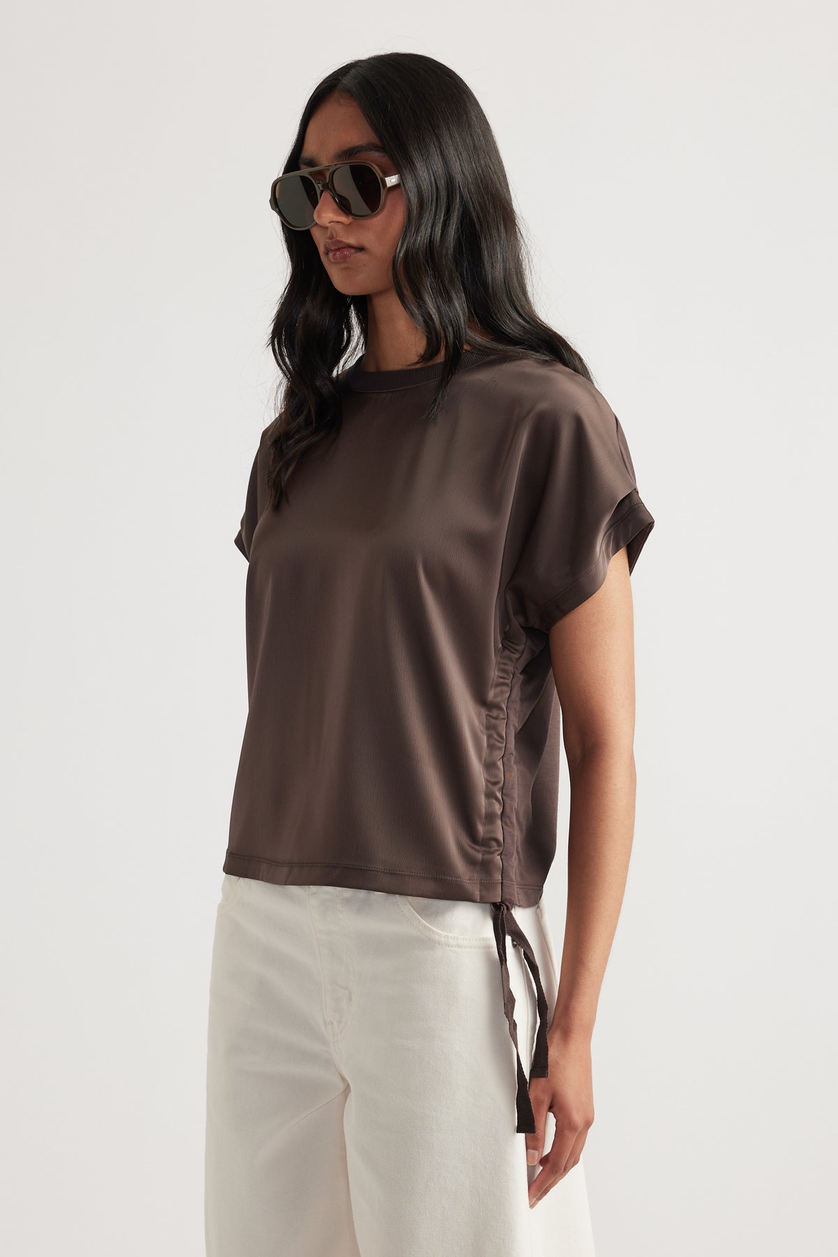 Woman wearing a relaxed fit short sleeve top with ruched side tie detail paired with light-colored wide-leg pants