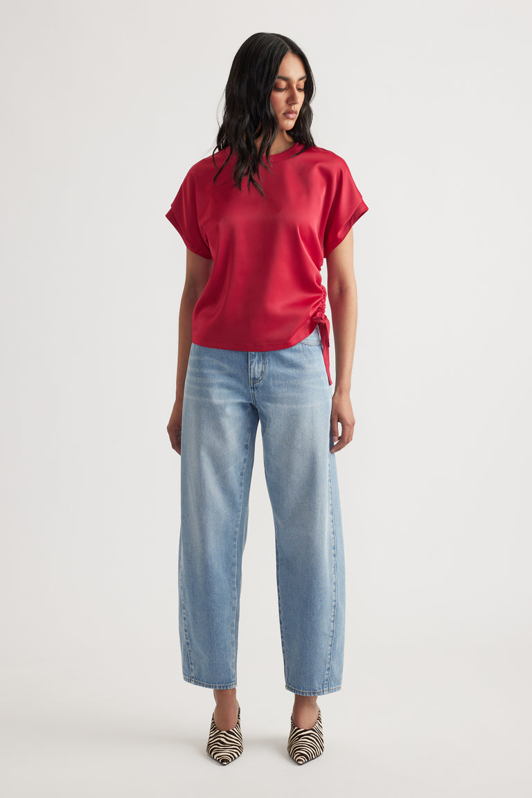 Woman wearing a relaxed red top with side tie detail paired with light wash straight-leg jeans and patterned heels