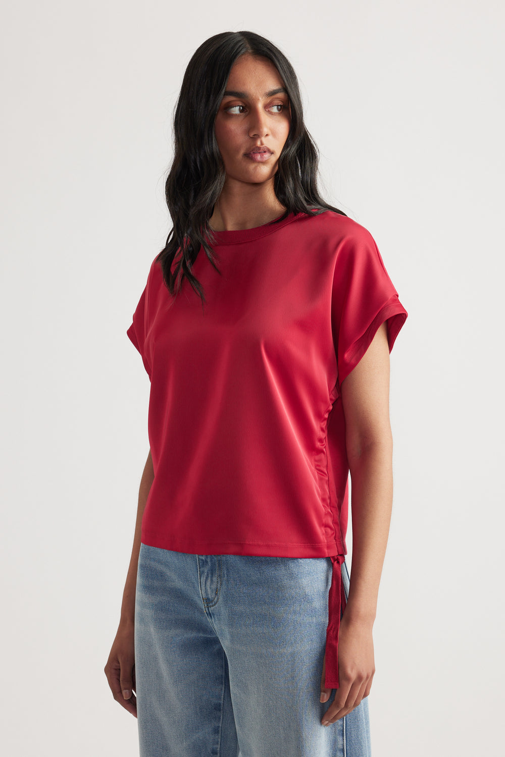 Woman wearing a relaxed fit red satin top with side tie detail paired with light blue casual denim jeans