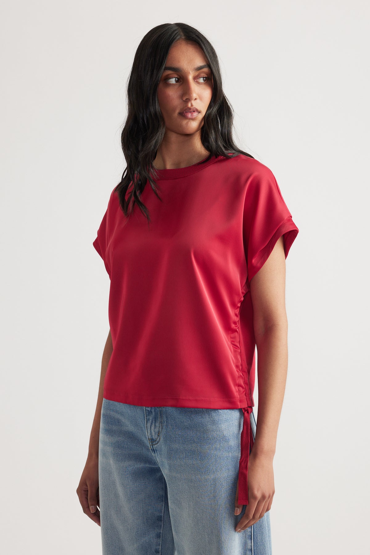 Woman wearing a relaxed fit red satin top with side tie detail paired with light blue casual denim jeans