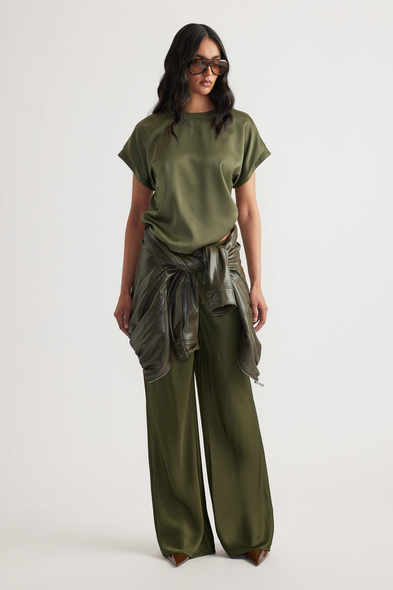 Woman wearing olive green relaxed fit satin top with matching wide-leg pants and leather jacket tied at waist