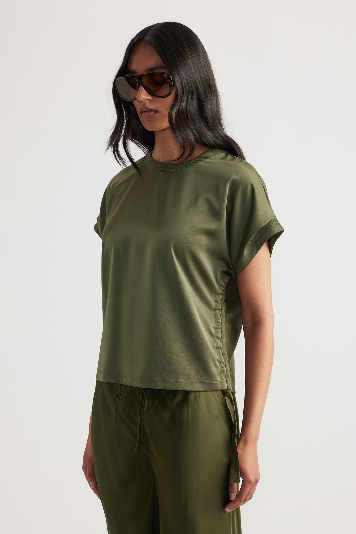 Woman wearing an olive green relaxed fit top with side tie detail and matching loose pants, paired with oversized sunglasses