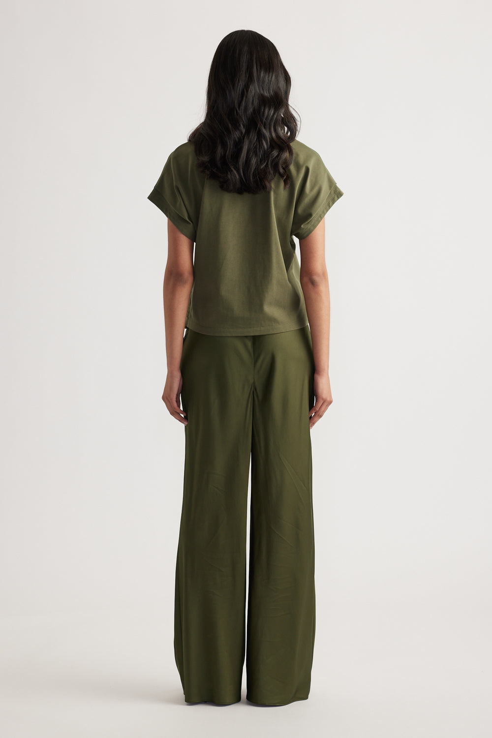 Rear view of woman wearing relaxed fit olive green short sleeve top and wide-leg pants against white background