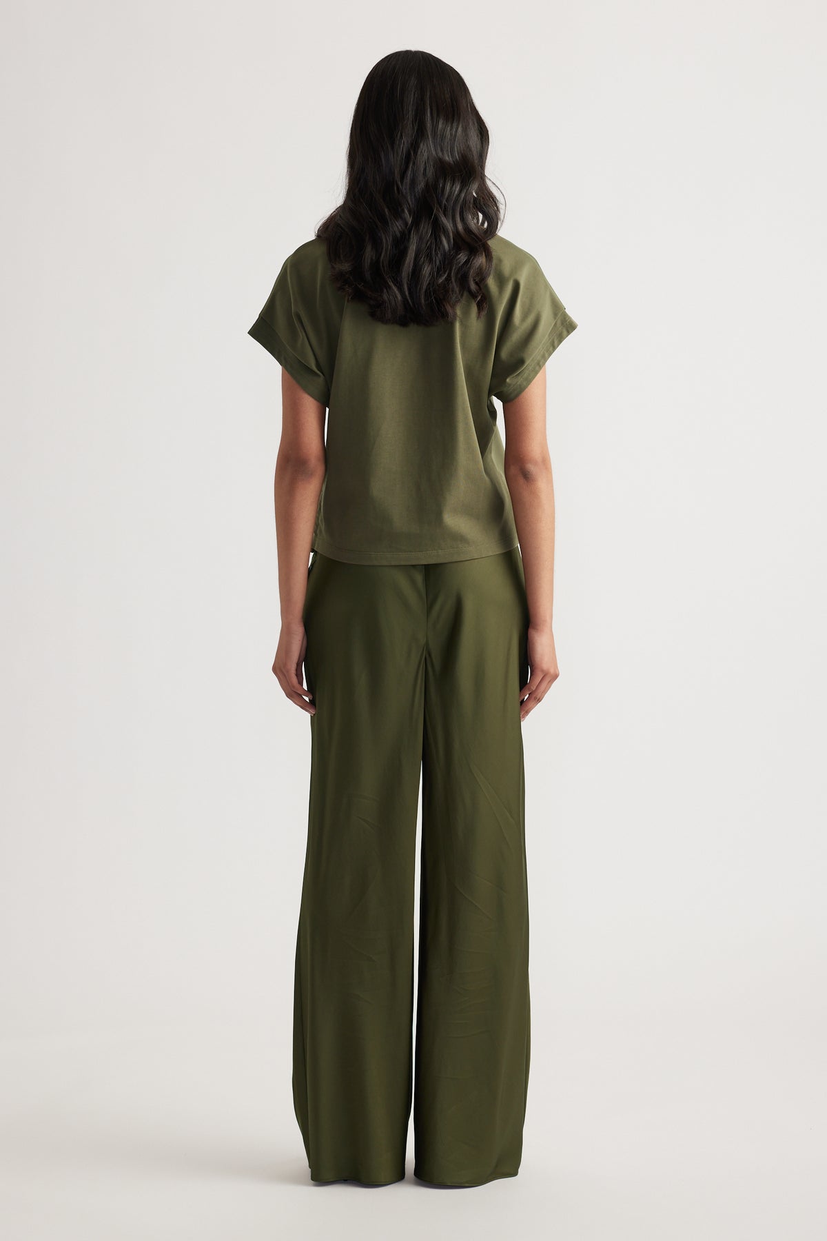 Rear view of woman wearing relaxed fit olive green short sleeve top and wide-leg pants against white background
