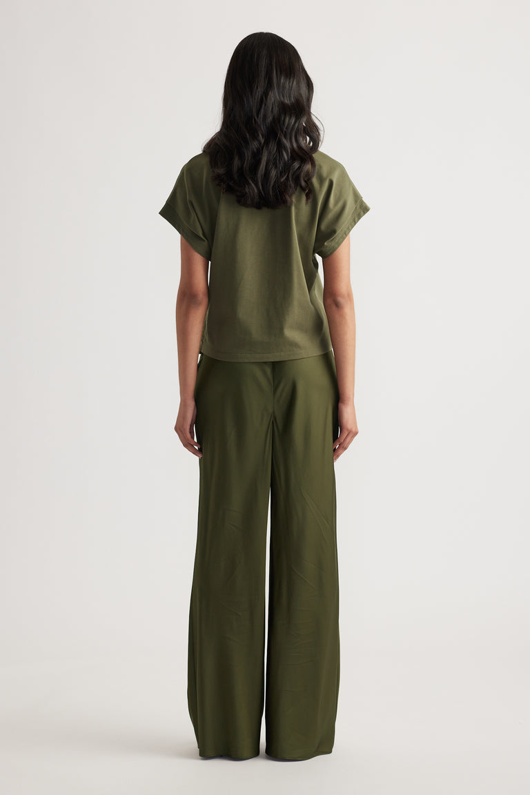 Rear view of woman wearing relaxed fit olive green short sleeve top and wide-leg pants against white background