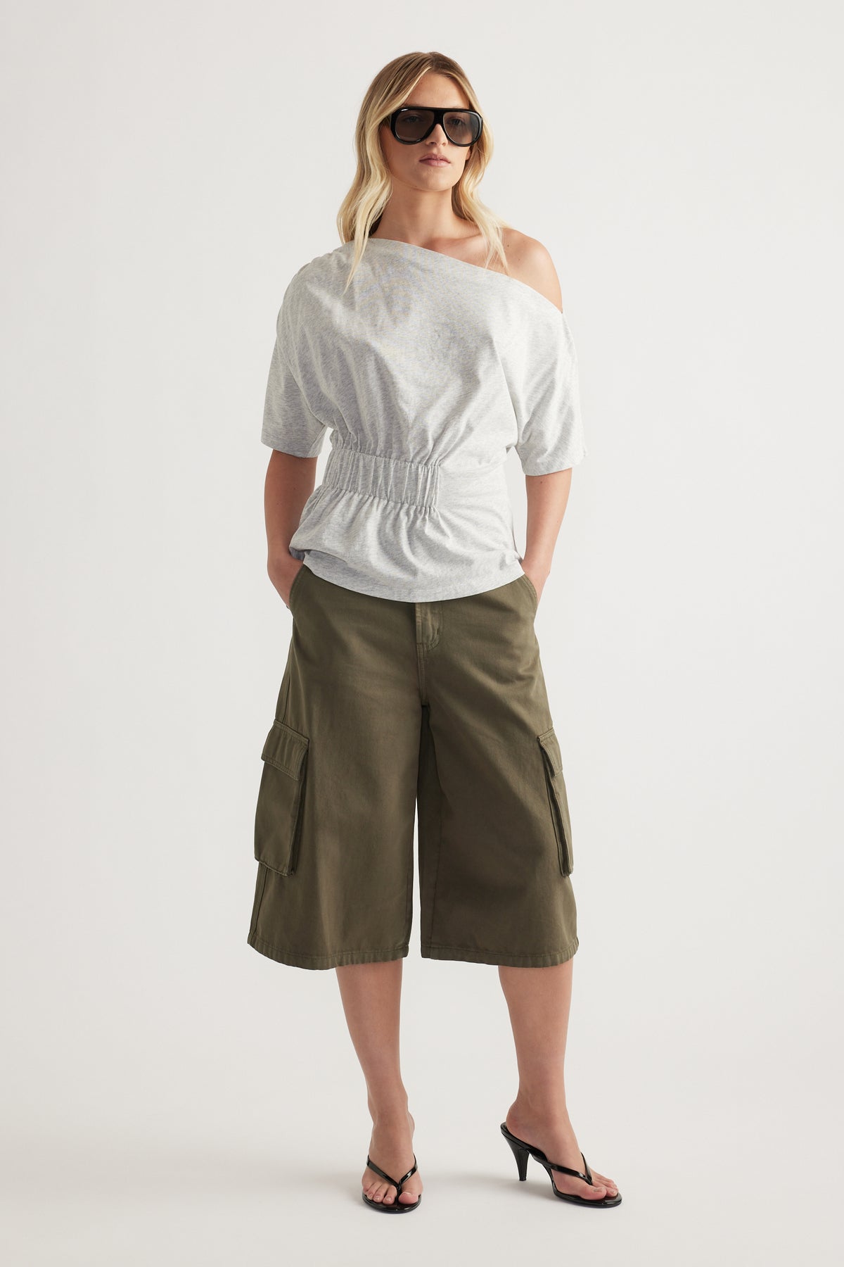 Woman wearing a white asymmetrical neckline tee with a cinched waist and olive cargo shorts