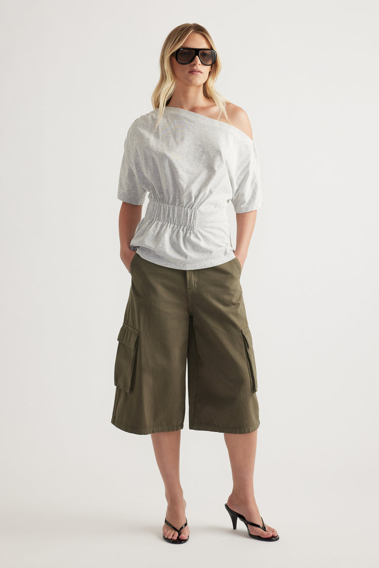 Woman wearing a white asymmetrical neckline tee with a cinched waist and olive cargo shorts