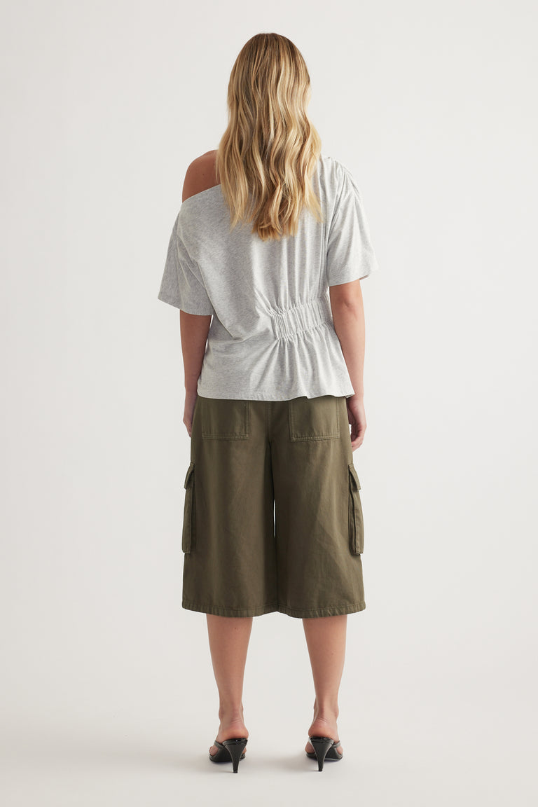 Back view of woman wearing a grey asymmetric tee with cinched waist and olive cargo shorts