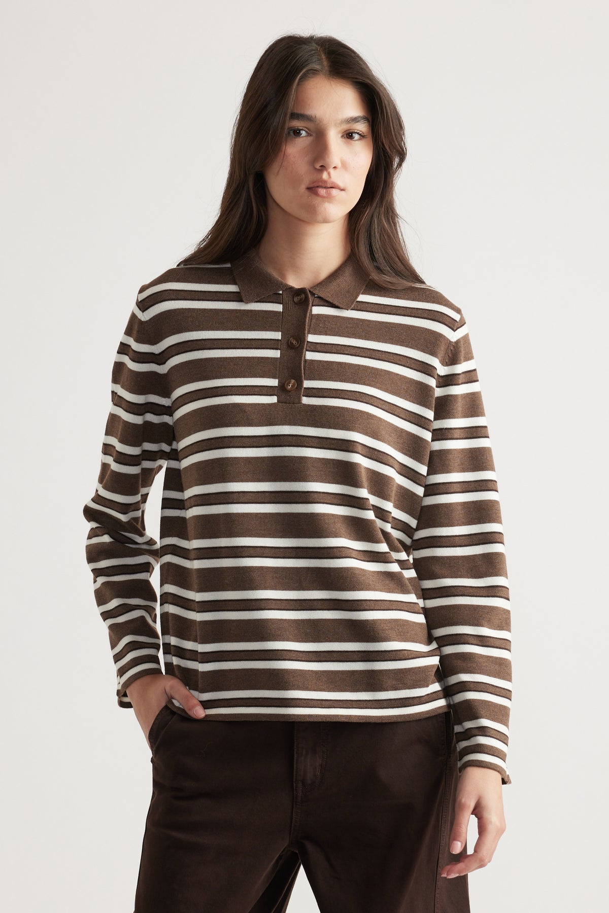 Woman wearing a brown and cream striped knit polo with long sleeves, styled casually with dark trousers