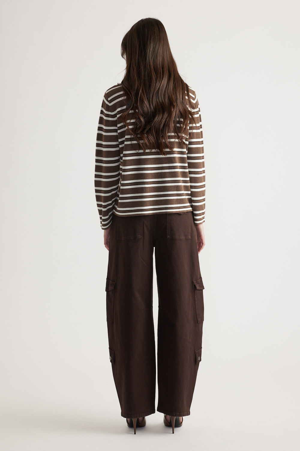 Woman wearing a brown and white striped long-sleeve knit top paired with loose dark brown cargo pants and heels