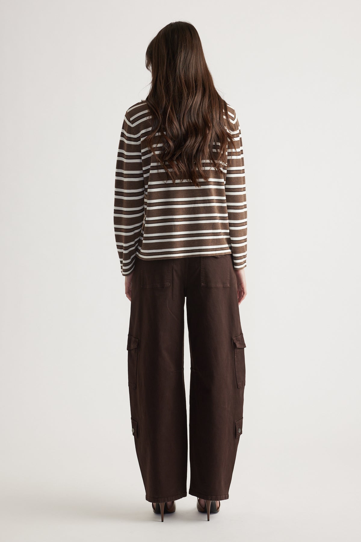Woman wearing a brown and white striped long-sleeve knit top paired with loose dark brown cargo pants and heels
