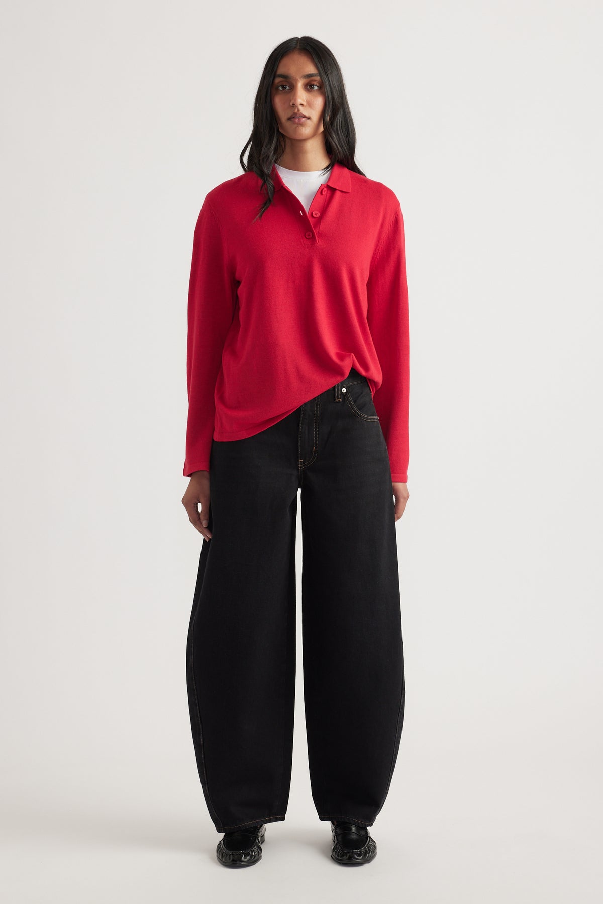 Woman wearing a crimson long-sleeve knit polo layered over white top paired with wide-leg black denim jeans and black shoes