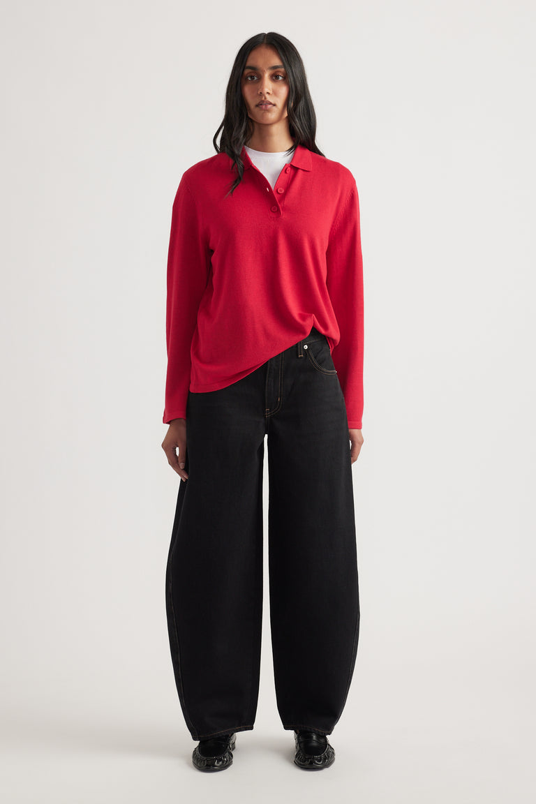 Woman wearing a crimson long-sleeve knit polo layered over white top paired with wide-leg black denim jeans and black shoes