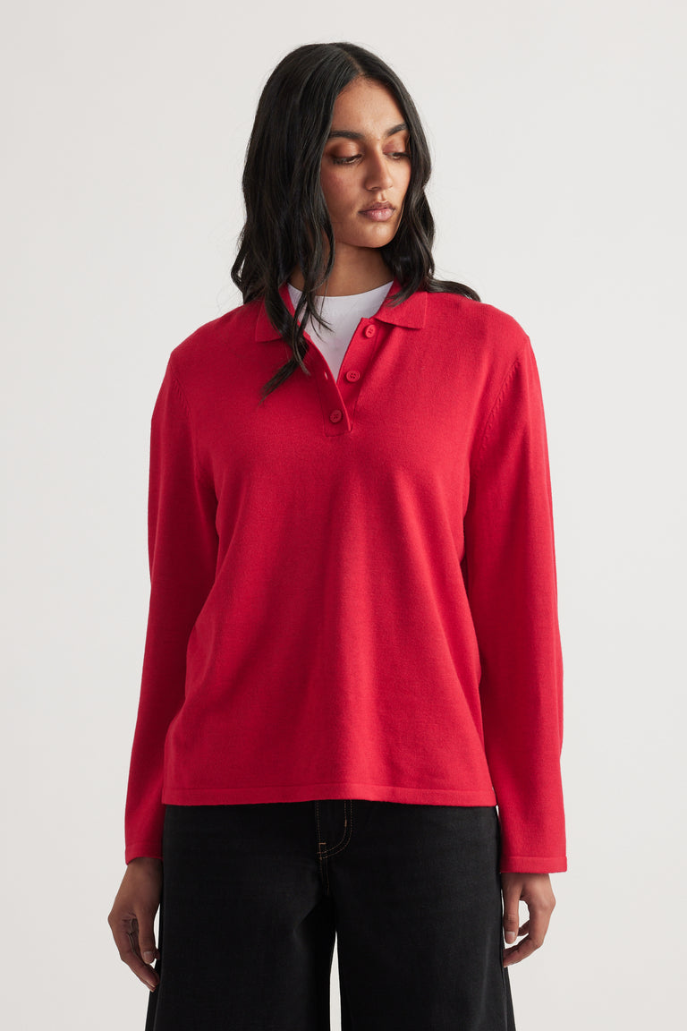 Woman wearing a bright red long-sleeve knit polo layered over a white top with loose black pants
