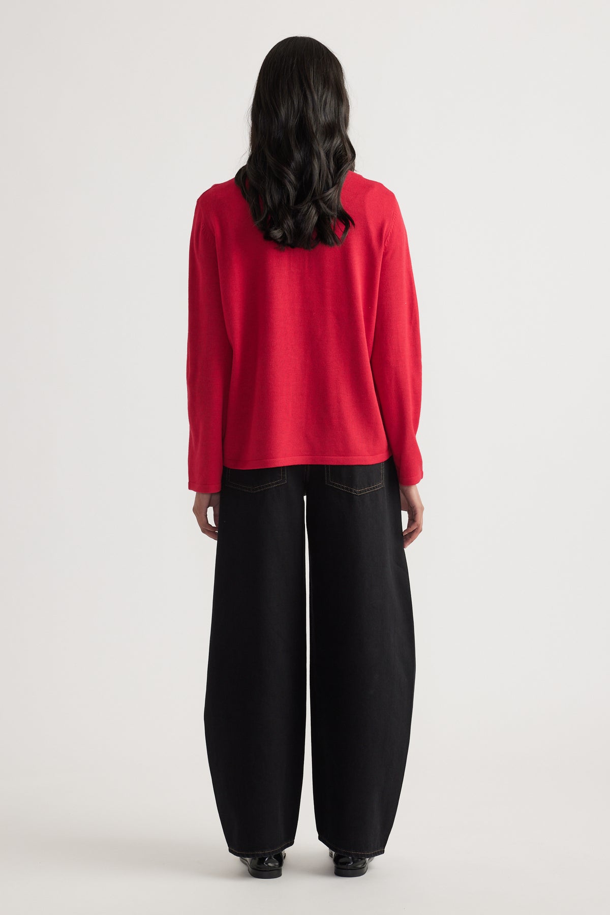 Woman seen from behind wearing a relaxed red knit polo paired with wide-leg black denim jeans and black shoes