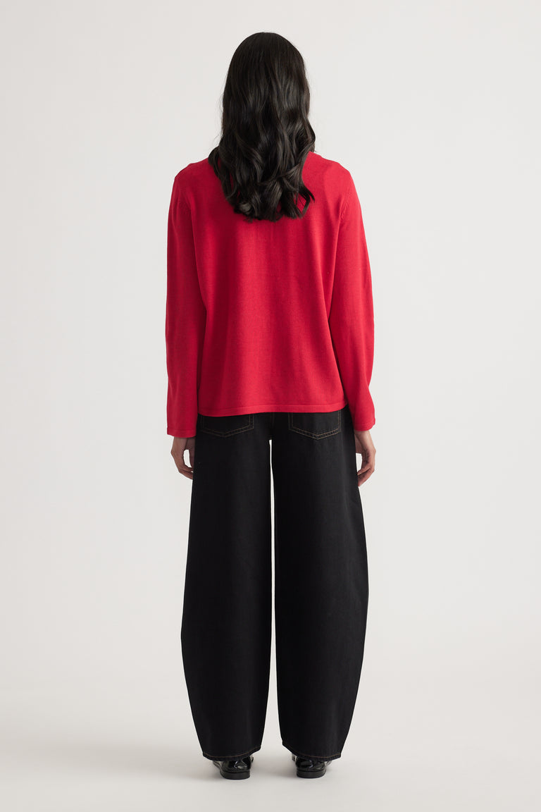 Woman seen from behind wearing a relaxed red knit polo paired with wide-leg black denim jeans and black shoes