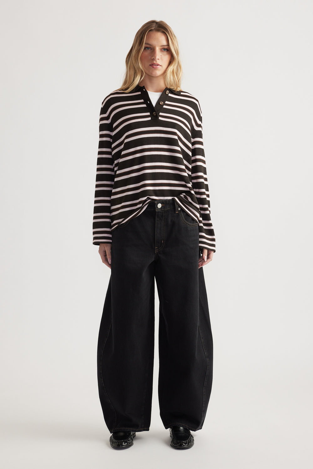 Woman wearing a striped knit polo with button details paired with wide-leg black denim jeans and black shoes