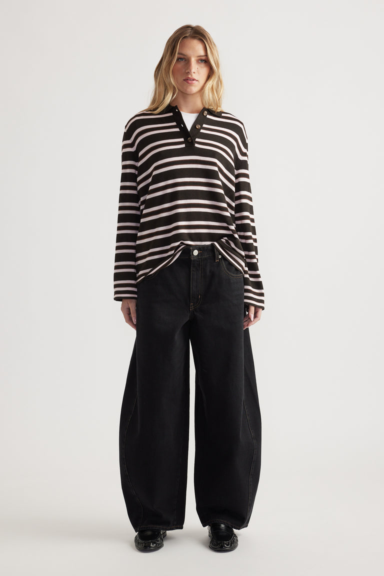 Woman wearing a striped knit polo with button details paired with wide-leg black denim jeans and black shoes