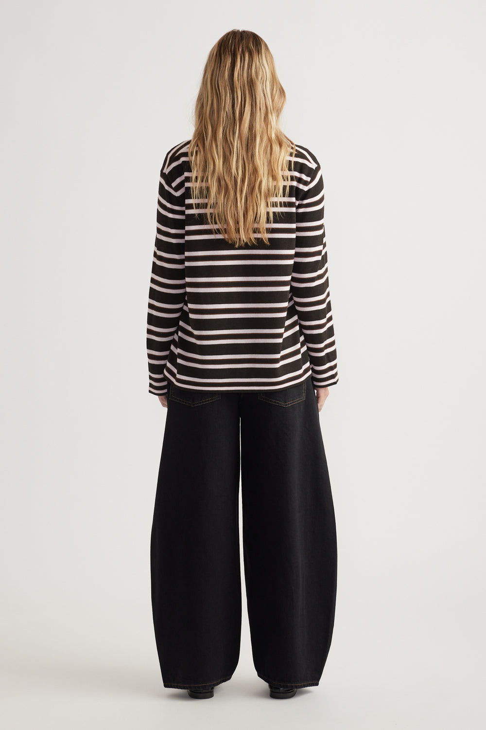 Woman seen from behind wearing a striped long sleeve knit top paired with wide-leg black pants against a white background