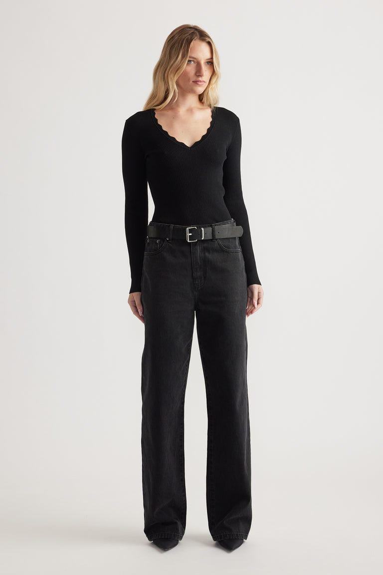 Woman wearing fitted black V-neck top with scalloped trim paired with high-waist wide-leg black jeans and belt