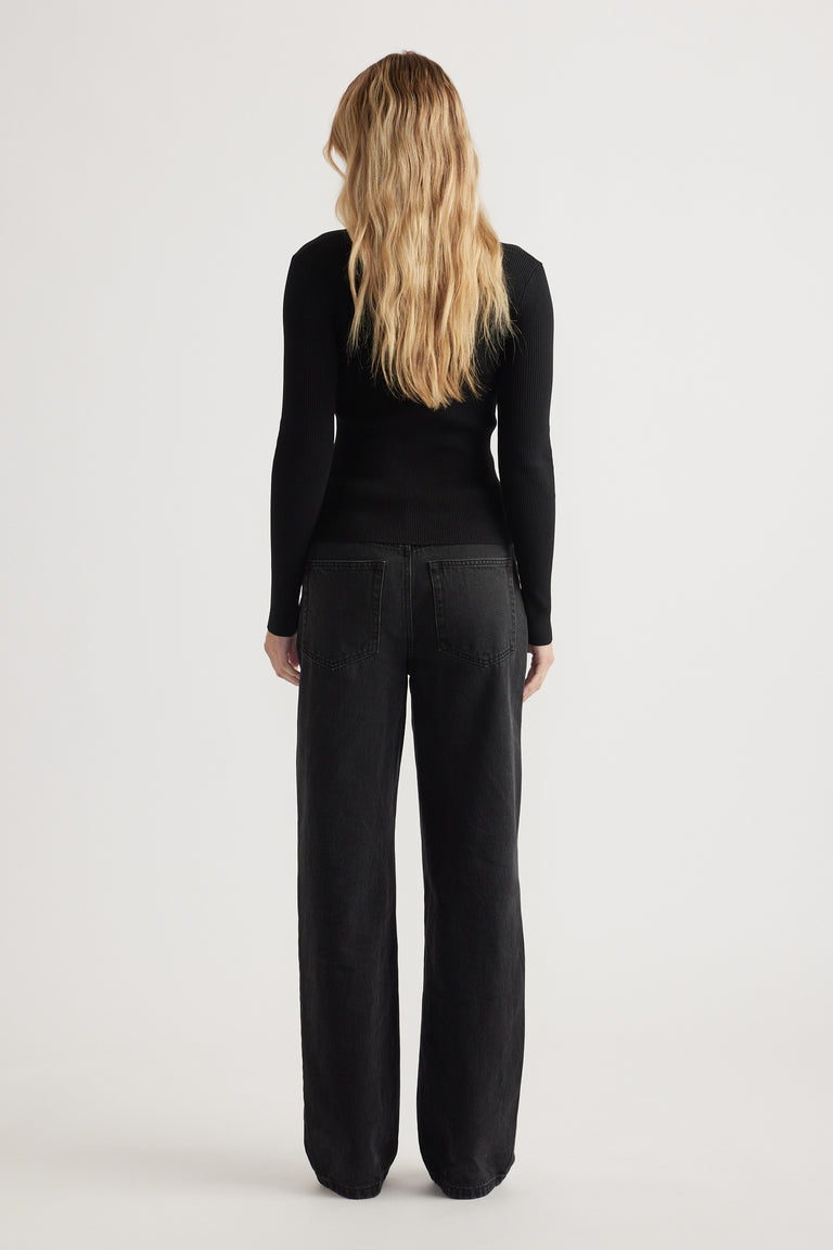 Woman seen from behind wearing a fitted black long sleeve top with ribbed texture and black wide-leg jeans