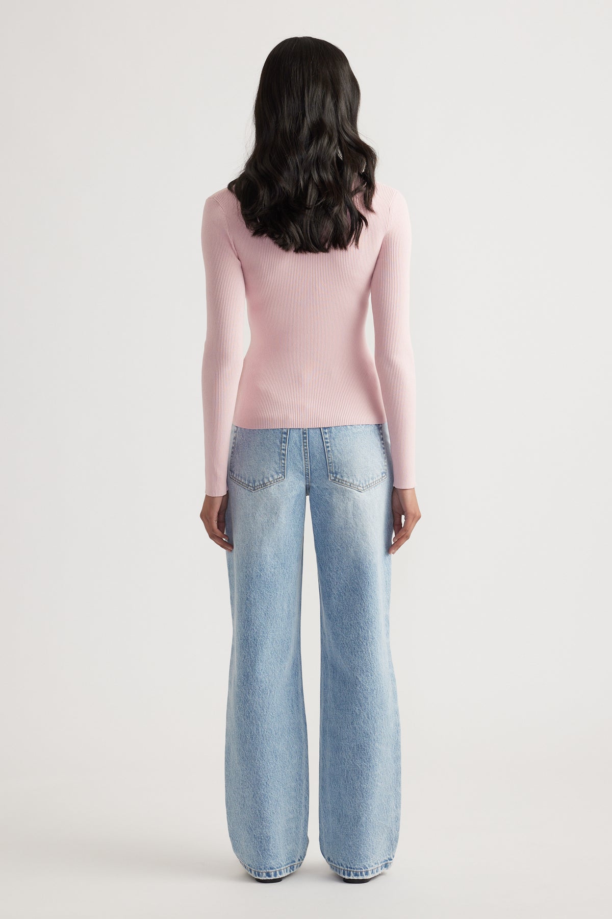 Woman shown from behind wearing a fitted light pink ribbed long sleeve top paired with loose light-wash jeans