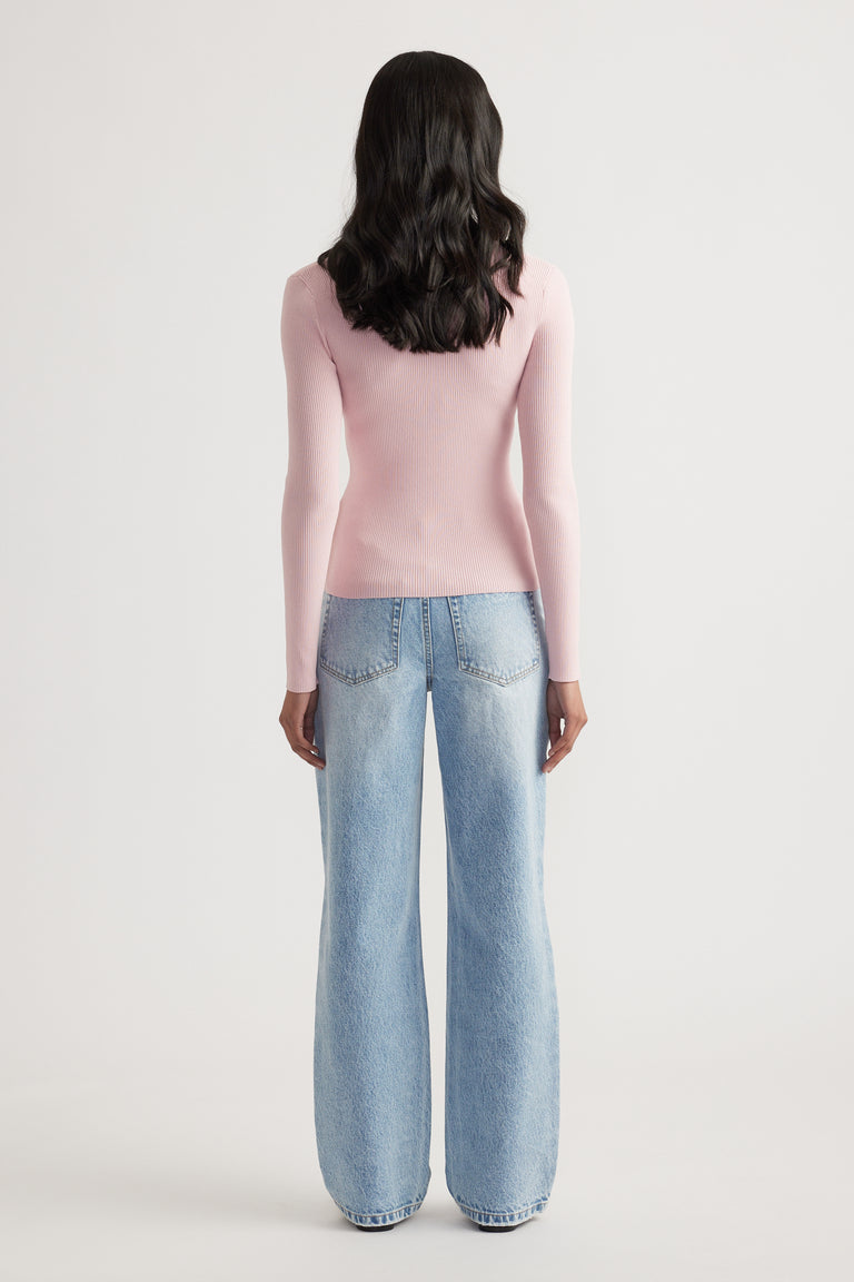 Woman shown from behind wearing a fitted light pink ribbed long sleeve top paired with loose light-wash jeans