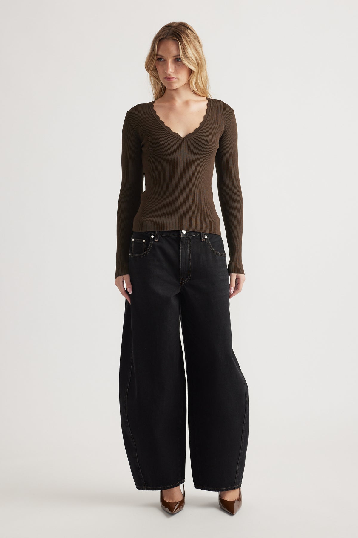 Woman wearing fitted ribbed V-neck top with scallop trim paired with wide-leg black jeans and pointed heels