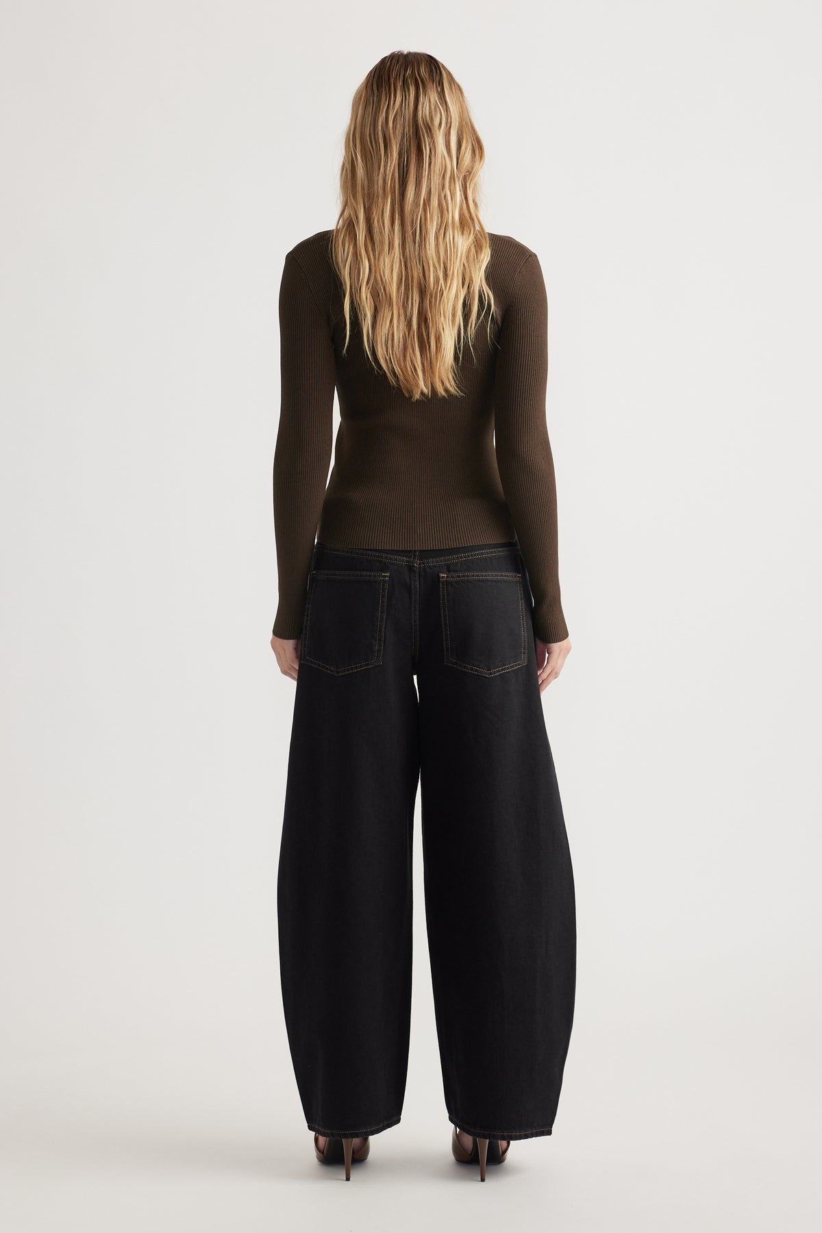 Woman seen from behind wearing a fitted dark brown long-sleeve top and wide-leg black jeans with heels