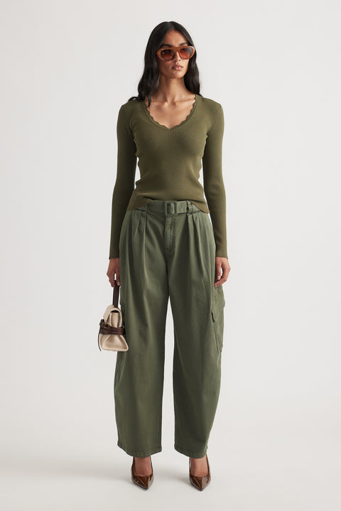 Woman wearing fitted ribbed olive green V-neck long sleeve top with scalloped trim paired with belted wide-leg pants