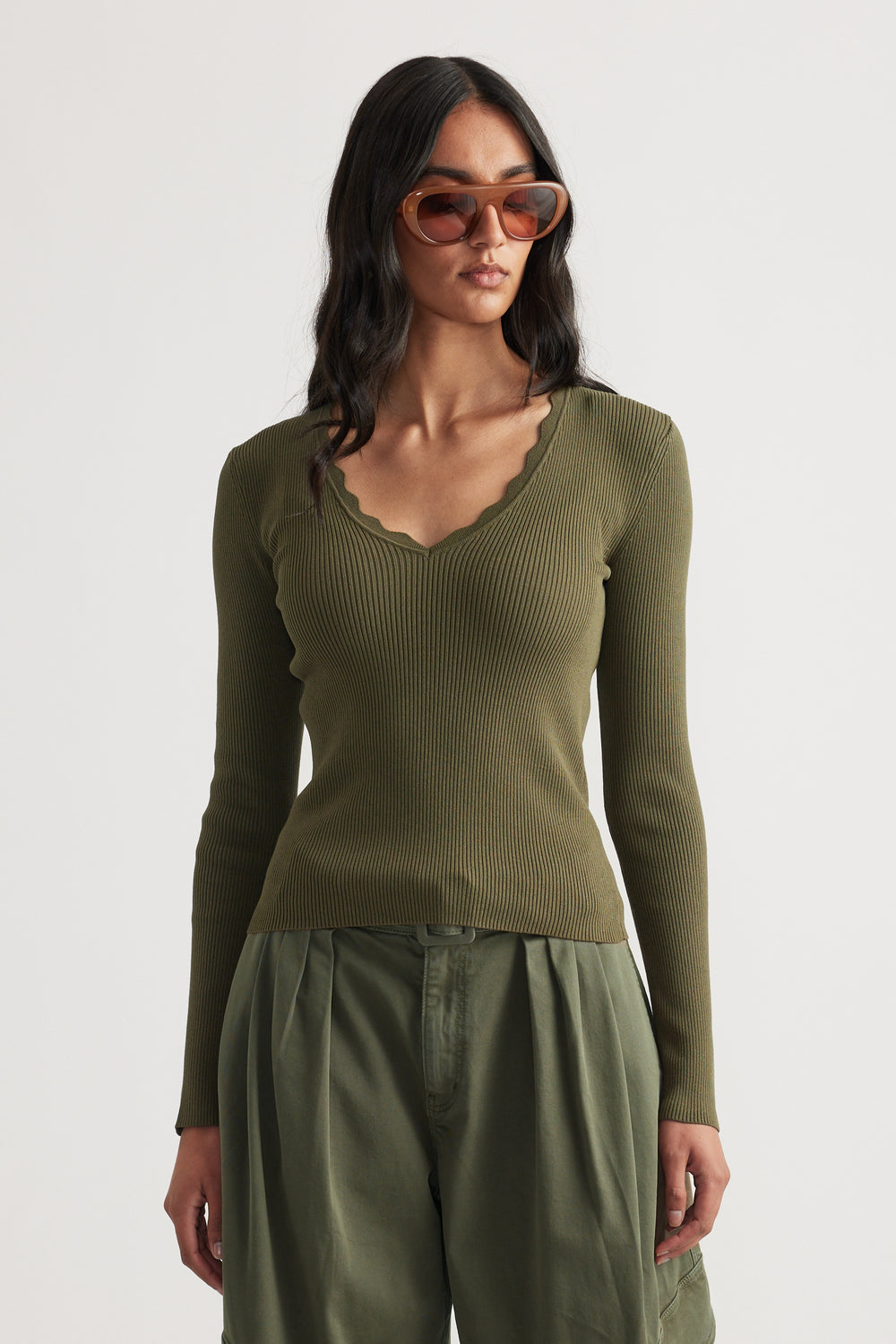 Woman wearing fitted ribbed olive green long sleeve top with scalloped V-neck and relaxed khaki pants
