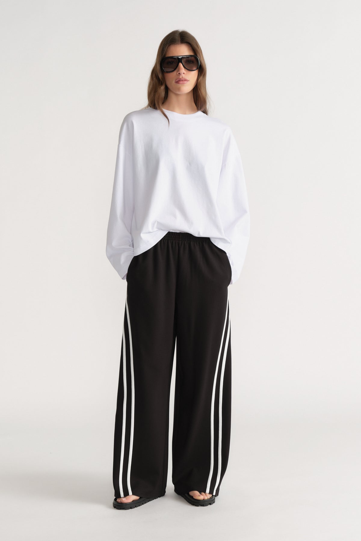 Woman wearing an oversized white long sleeve tee with black wide leg side stripe pants and sunglasses