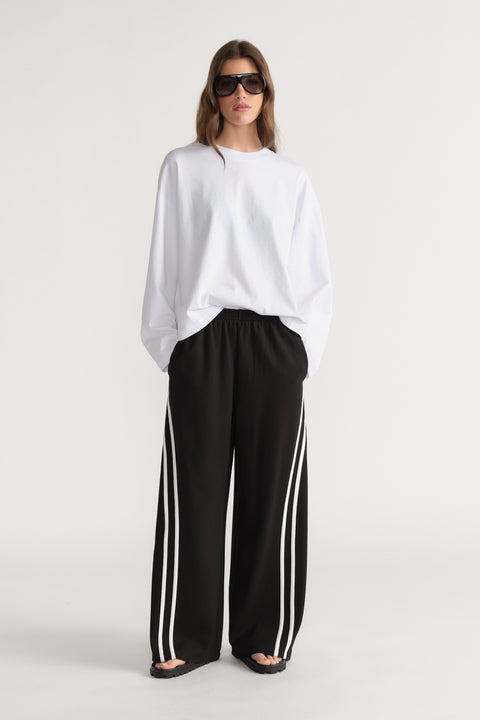Woman wearing an oversized white long sleeve tee with black wide leg side stripe pants and sunglasses