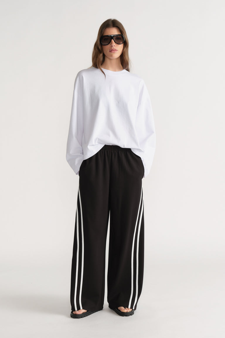 Woman wearing an oversized white long sleeve tee with black wide leg side stripe pants and sunglasses