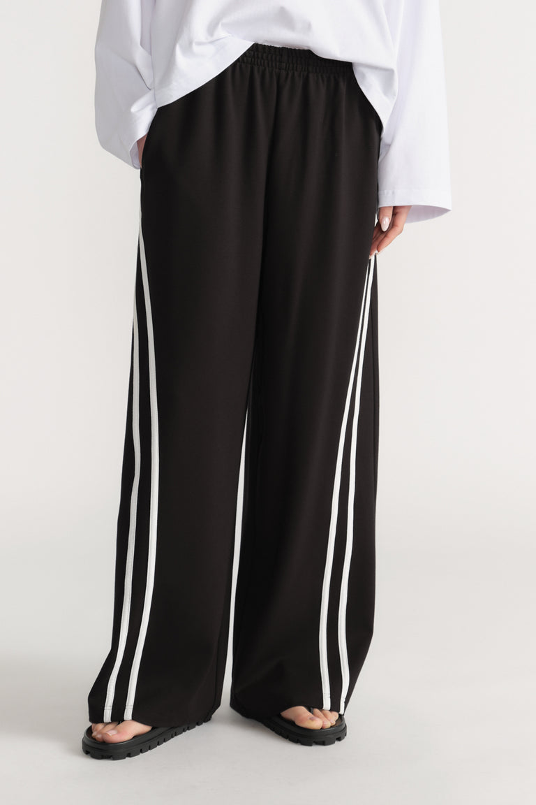 Woman wearing black wide leg pants with double white side stripes, a white shirt and sandals