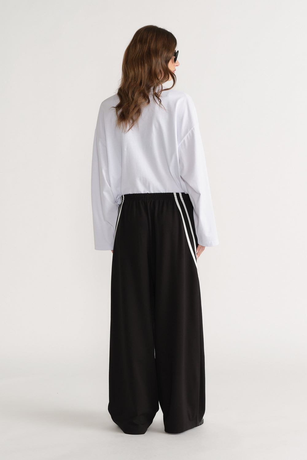 Model viewed from behind wearing black wide leg side stripe pants with a white shirt and sunglasses