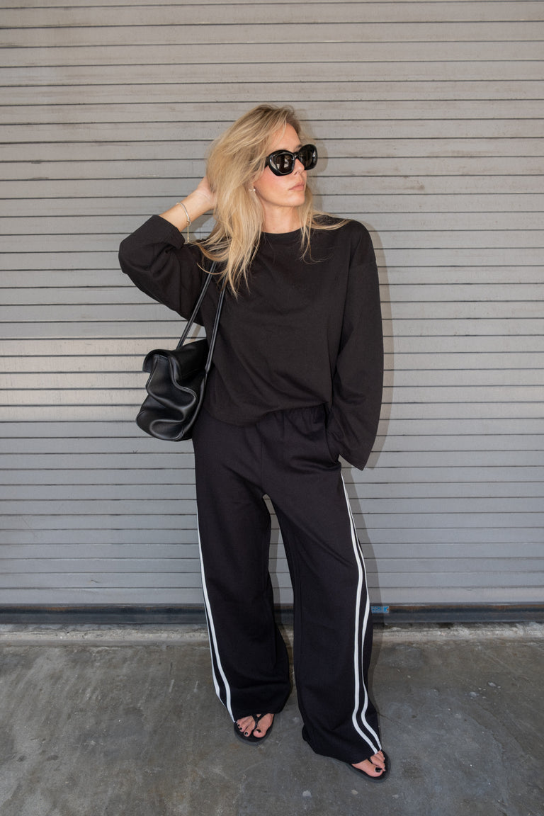 Woman wearing a black oversized top and wide leg pants with white side stripes and sunglasses