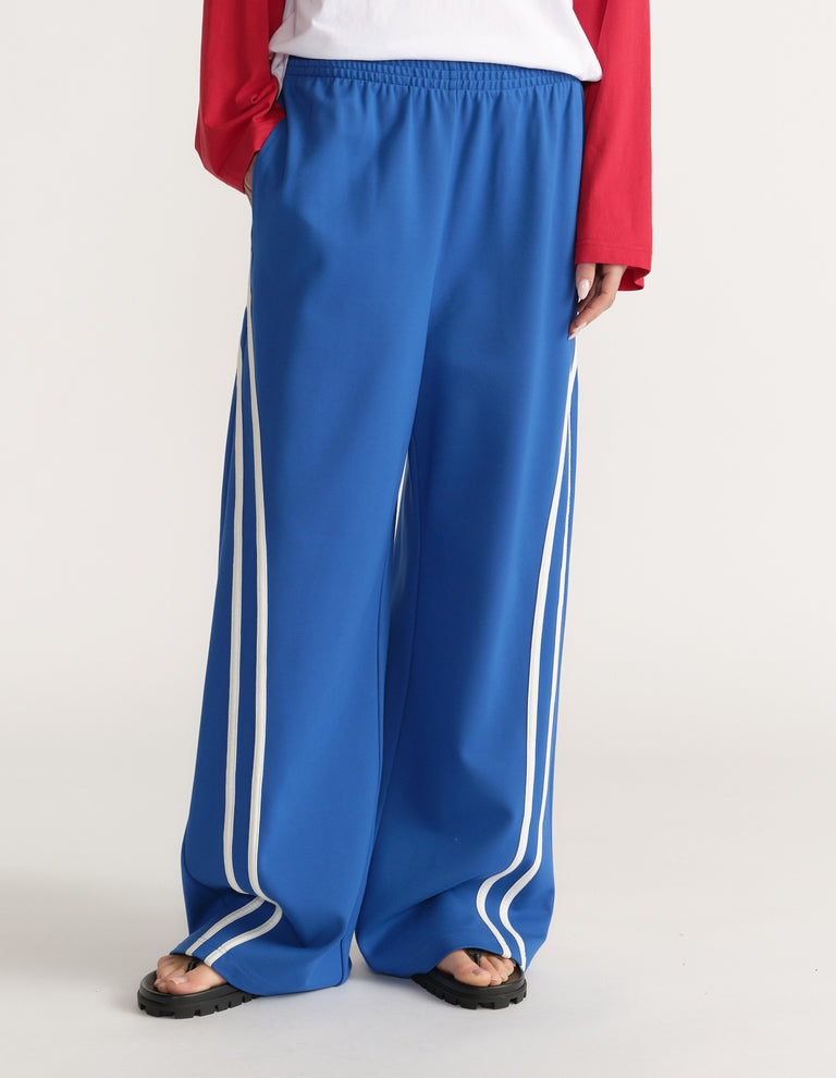 Woman wearing blue wide leg pants with white side stripes, a white tee, red long sleeve top and sandals