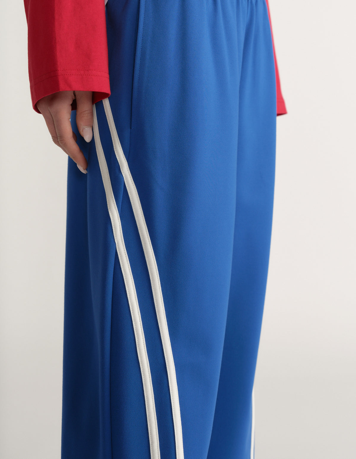 Woman wearing blue wide leg pants with double white side stripes and a red long sleeve top