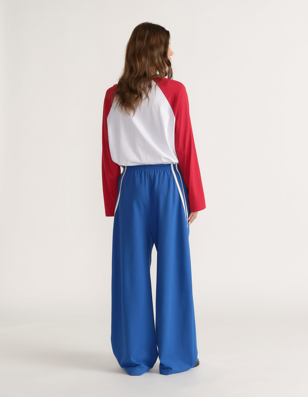 Woman viewed from behind wearing blue wide leg pants with white side stripes and a white and red long sleeve top