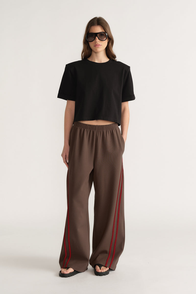 Woman in a black cropped tee and brown wide leg pants with red side stripes and sunglasses