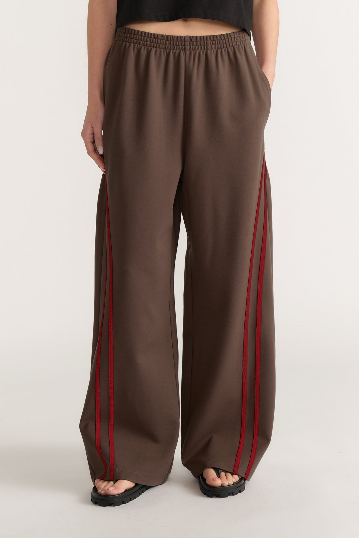 Woman wearing brown wide leg pants with red side stripes, an elastic waist and black sandals