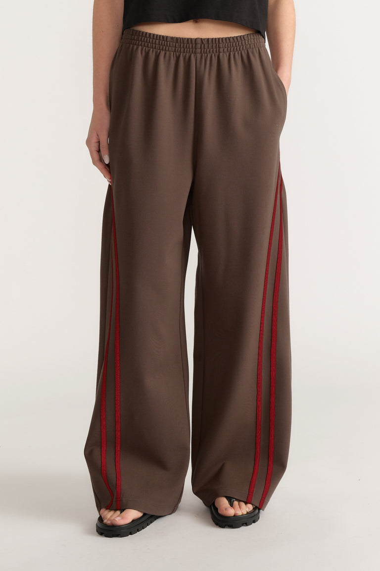 Woman wearing brown wide leg pants with red side stripes, an elastic waist and black sandals