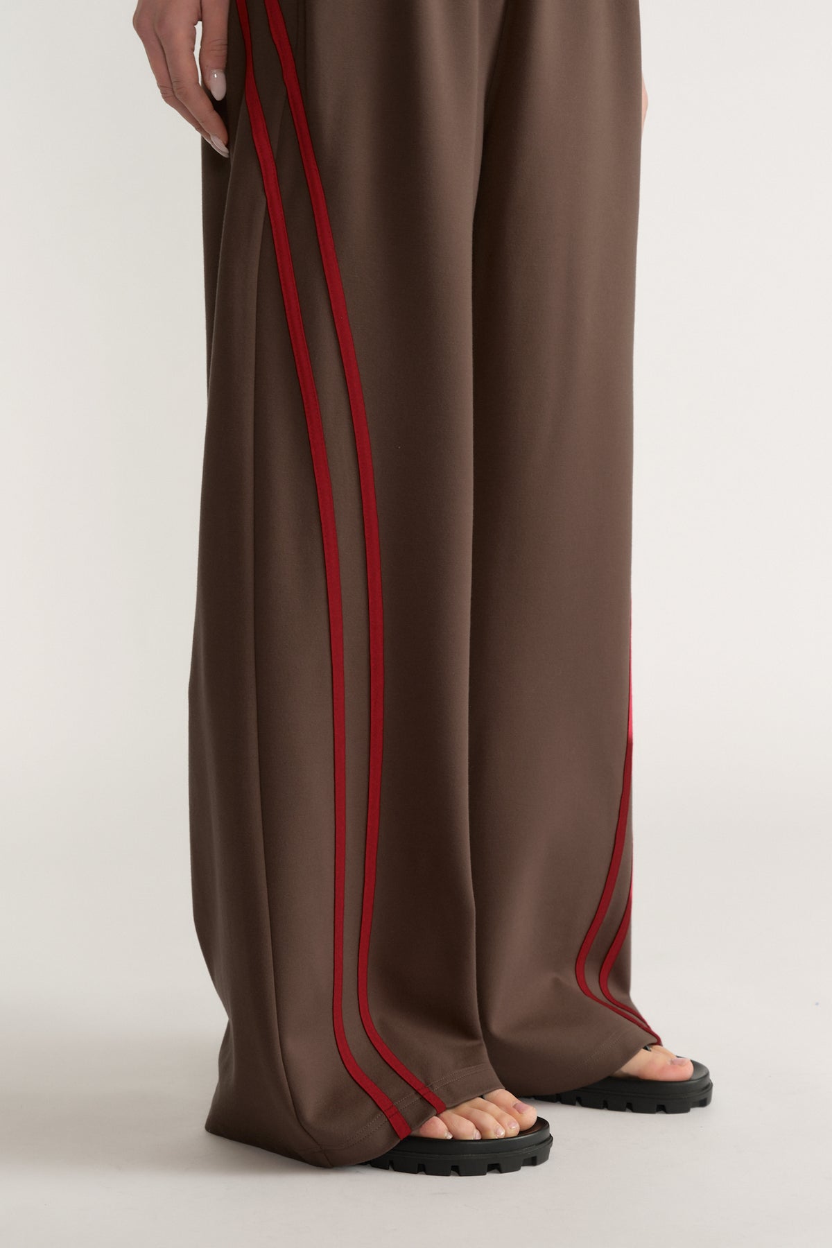 Woman wearing brown wide leg pants with red side stripes and black sandals