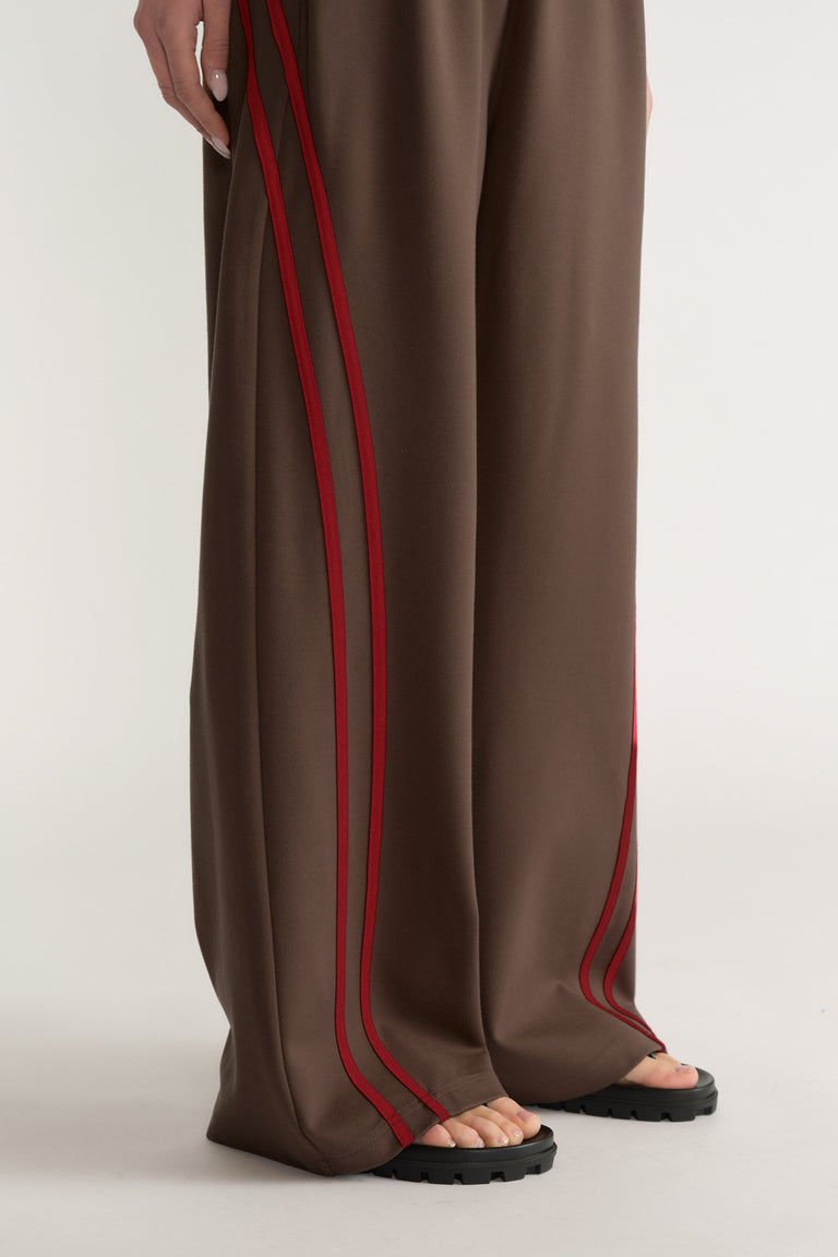 Woman wearing brown wide leg pants with red side stripes and black sandals