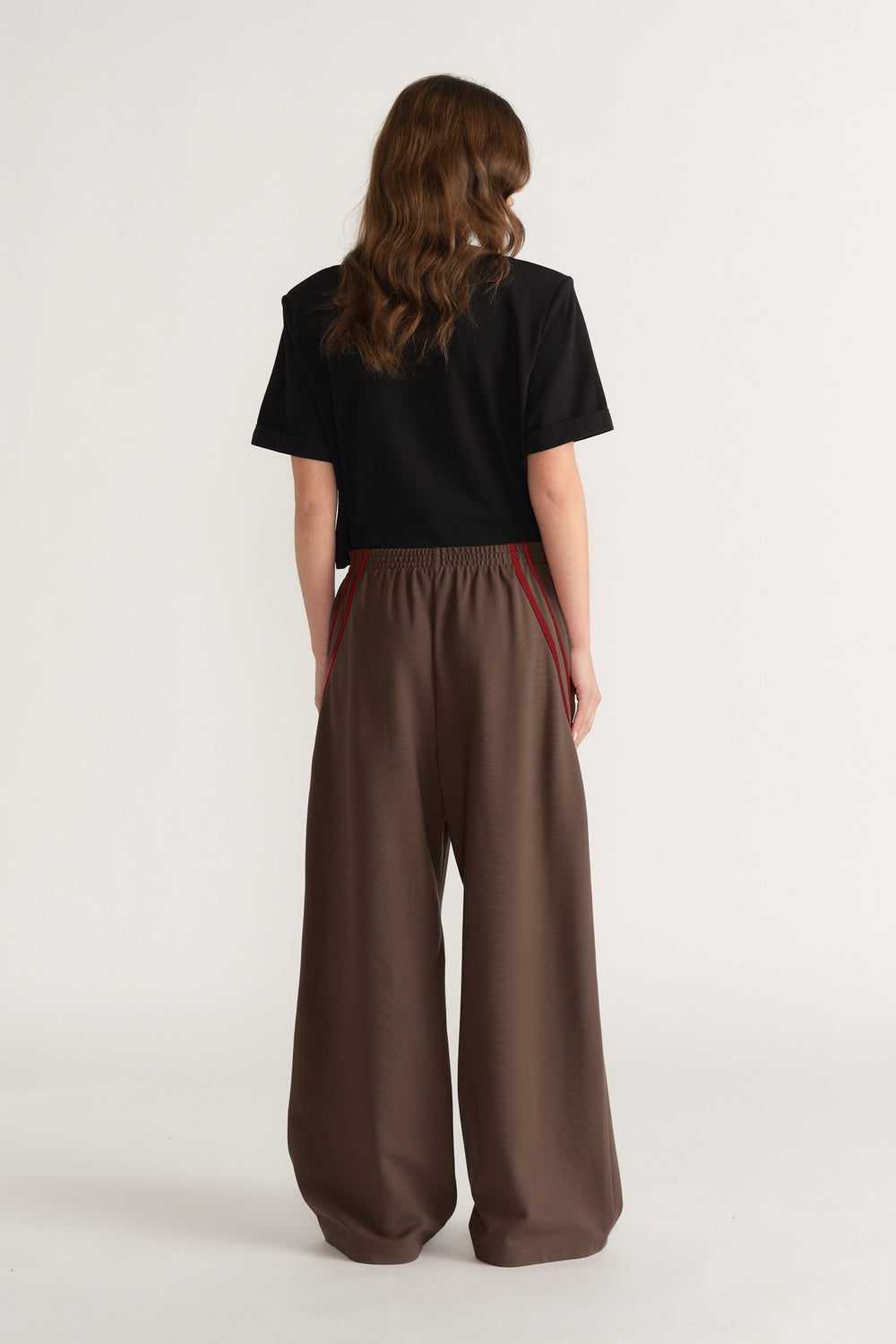 Woman viewed from behind wearing brown wide leg pants with red side stripes and a black tee