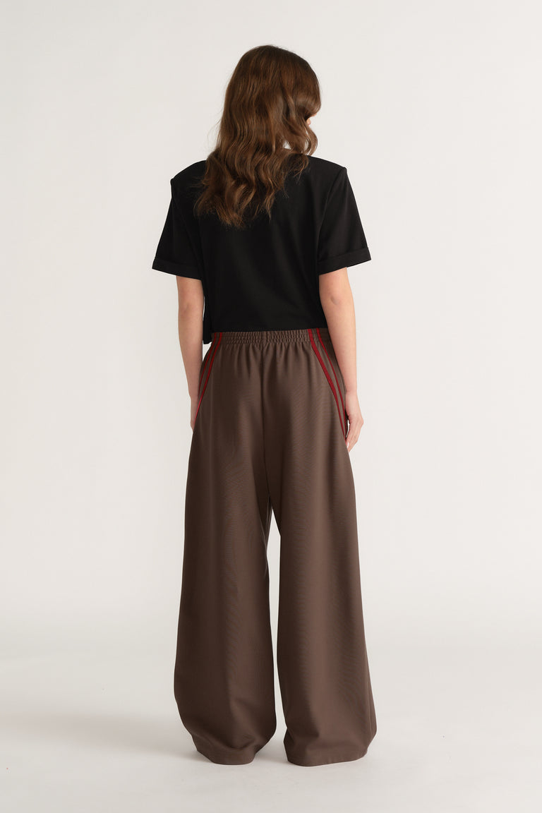 Woman viewed from behind wearing brown wide leg pants with red side stripes and a black tee