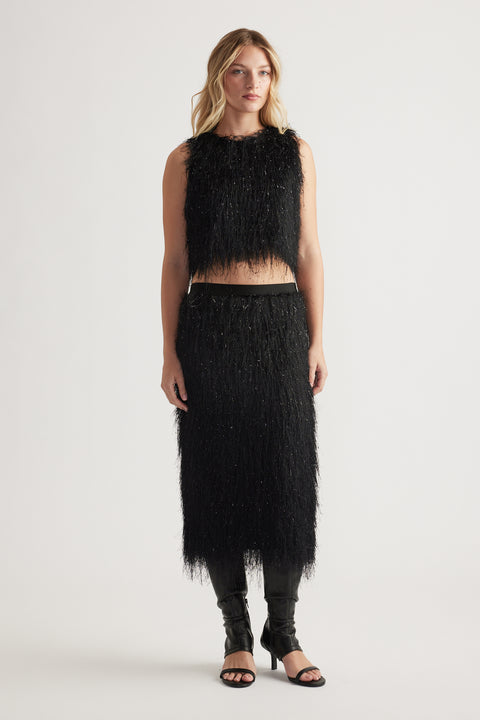 Woman wearing a black textured sleeveless top and matching midi skirt with subtle shimmer, paired with black open-toe heels