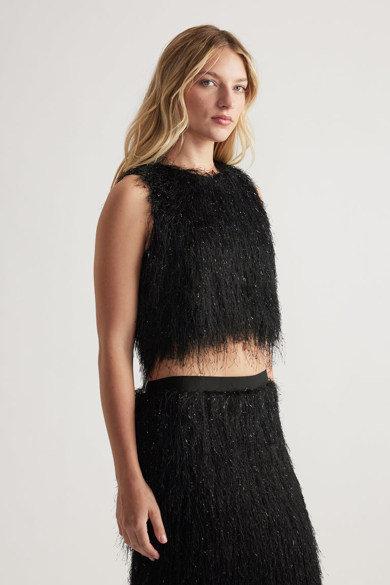 Woman wearing a sleeveless black fringed crop top paired with a matching textured skirt, styled simply and elegantly.